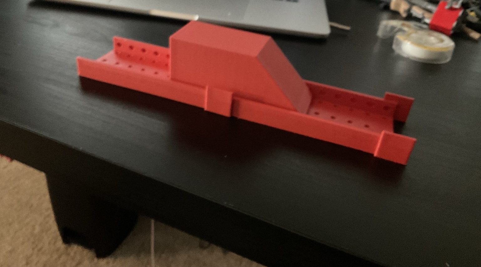 My printed V1 Magnarail: a red 3D-printed track piece with magnet holes and the red train sitting on it, on a desk.